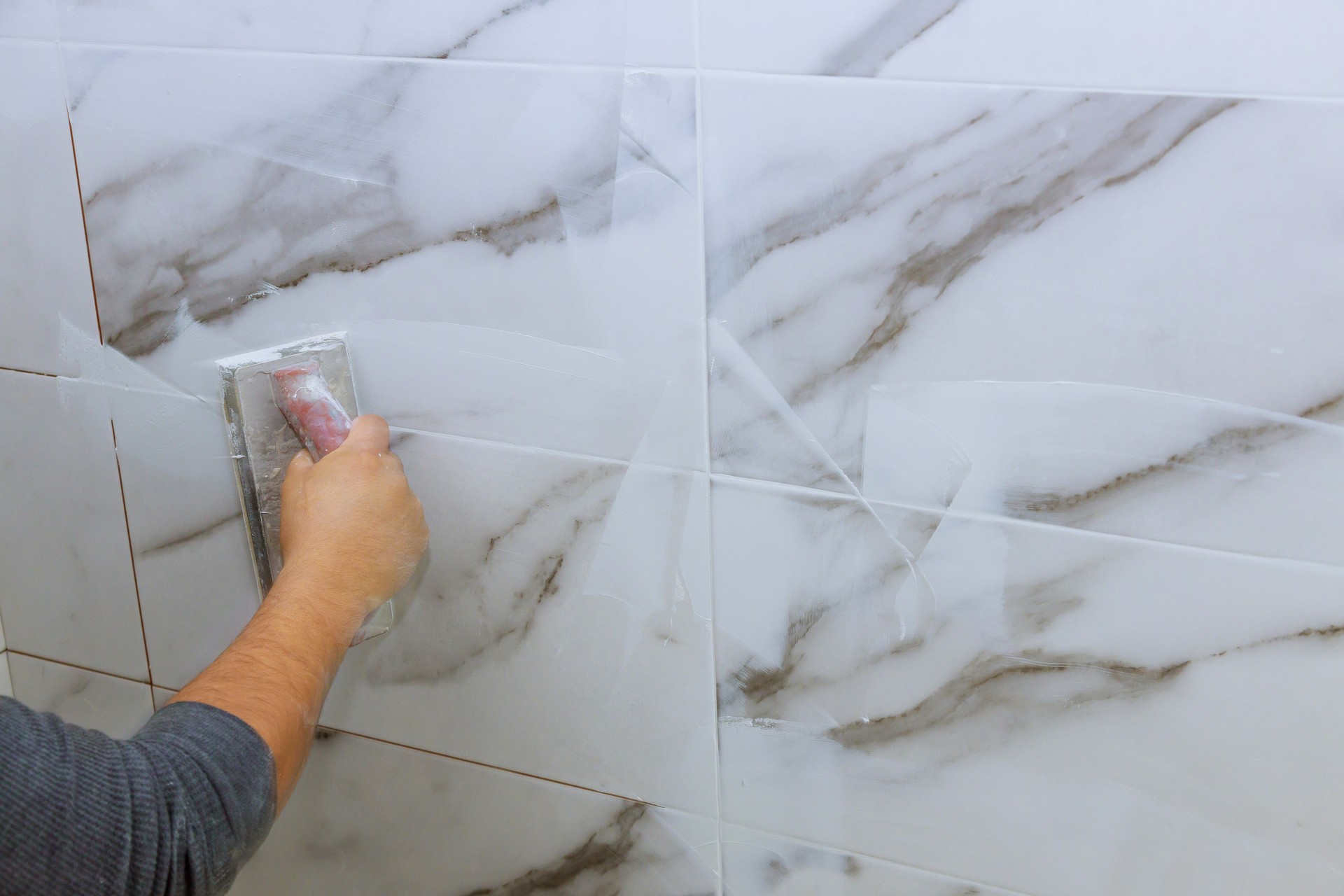 Male hand with the rubber applies grout on a seam between tiles